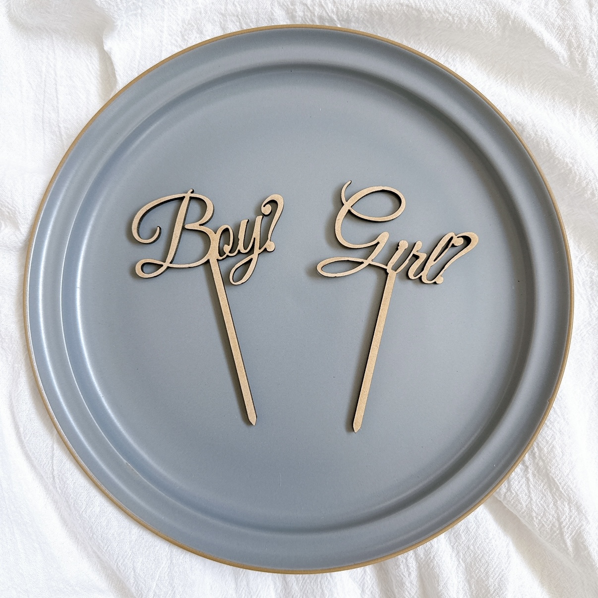 「Boy?」「Girl?」の木製ケーキトッパーをグレーのお皿に平置きした商品写真。木の質感がやさしく伝わる