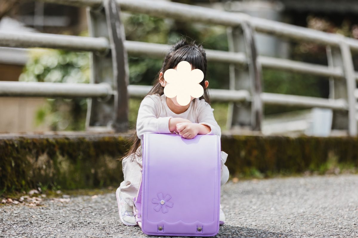 花の模様が入った薄紫のランドセルを前に置いて、しゃがんでいる娘