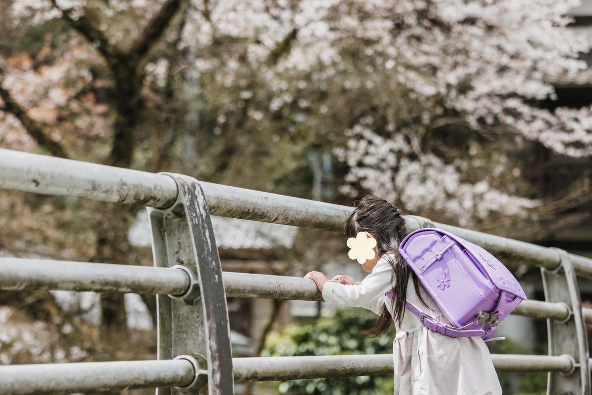 ランドセルを背負って、橋の手すりから外をのぞく娘