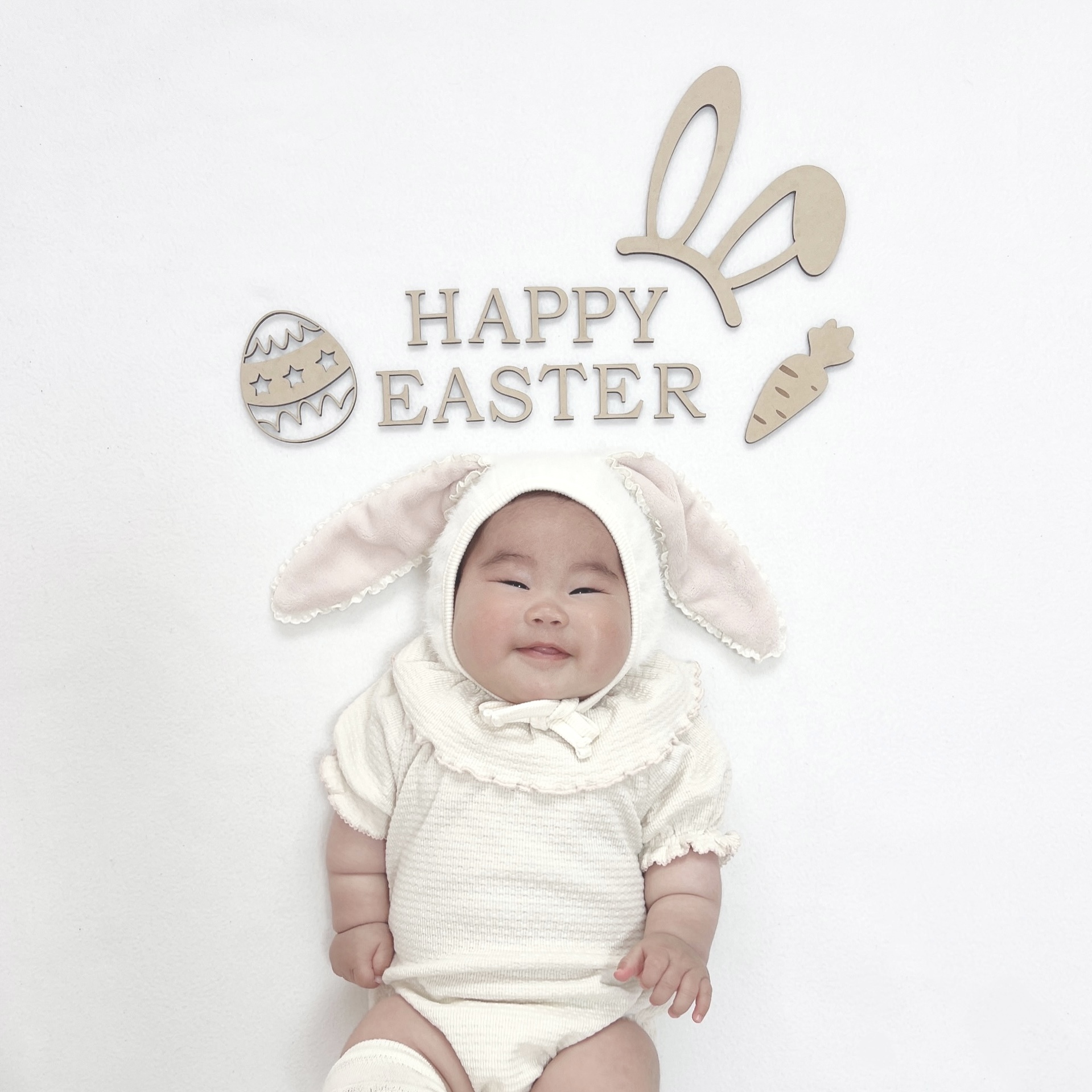 バニー衣装の赤ちゃんと「HAPPY EASTER」の木製バナー。こんな特別な日の1枚こそ、みてねで祖父母に届けたい写真です