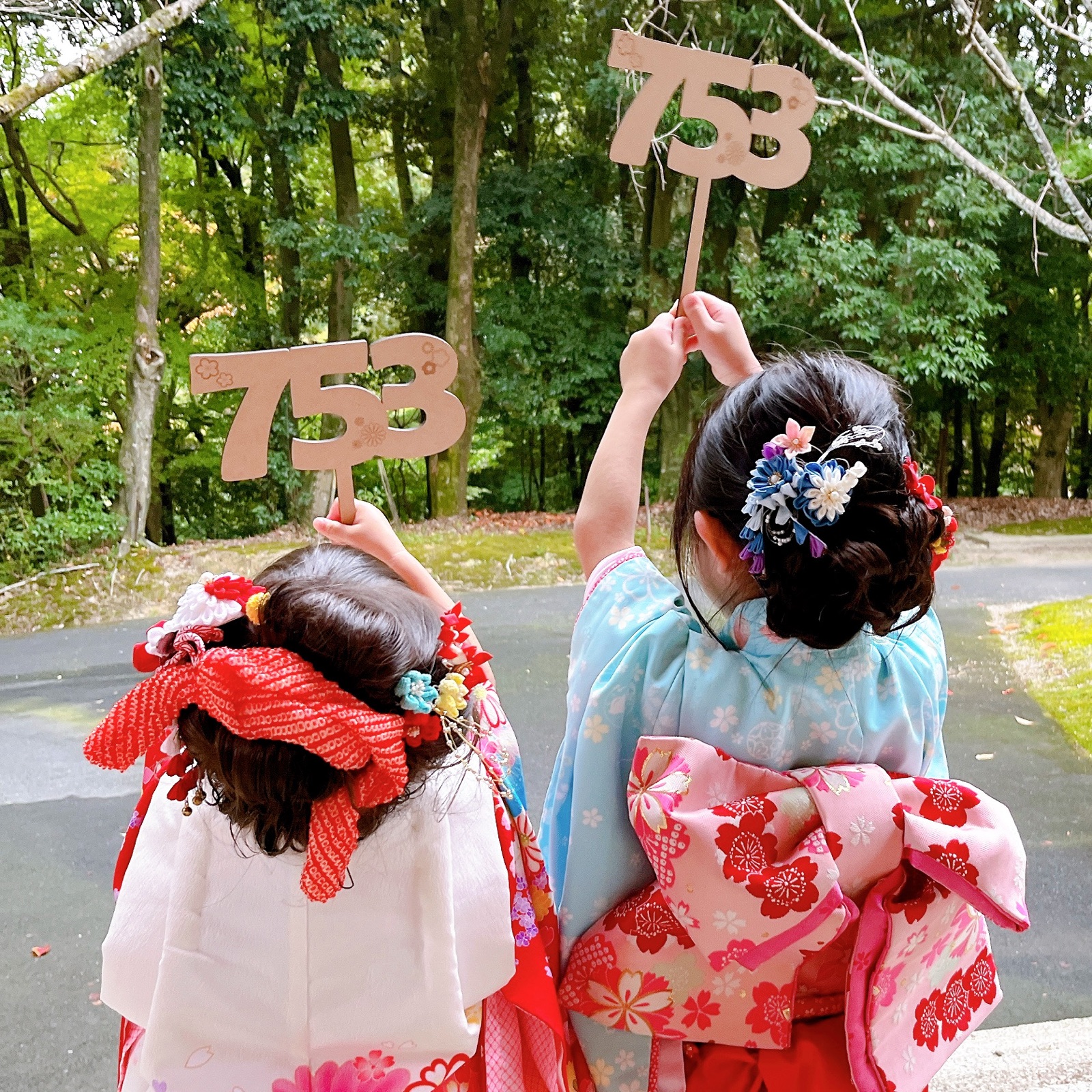 七五三の参道で753の木製スティックを掲げる姉妹の後ろ姿